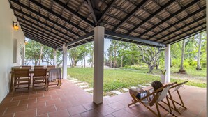 A covered patio with a table and chairs, a hammock, and a view of a garden. - Cashew Cashew Villa (Phu Quoc)