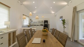 A modern kitchen with white cabinets, a dining table with wicker chairs, and pendant lights. - Cashew Cashew Villa (Phu Quoc)