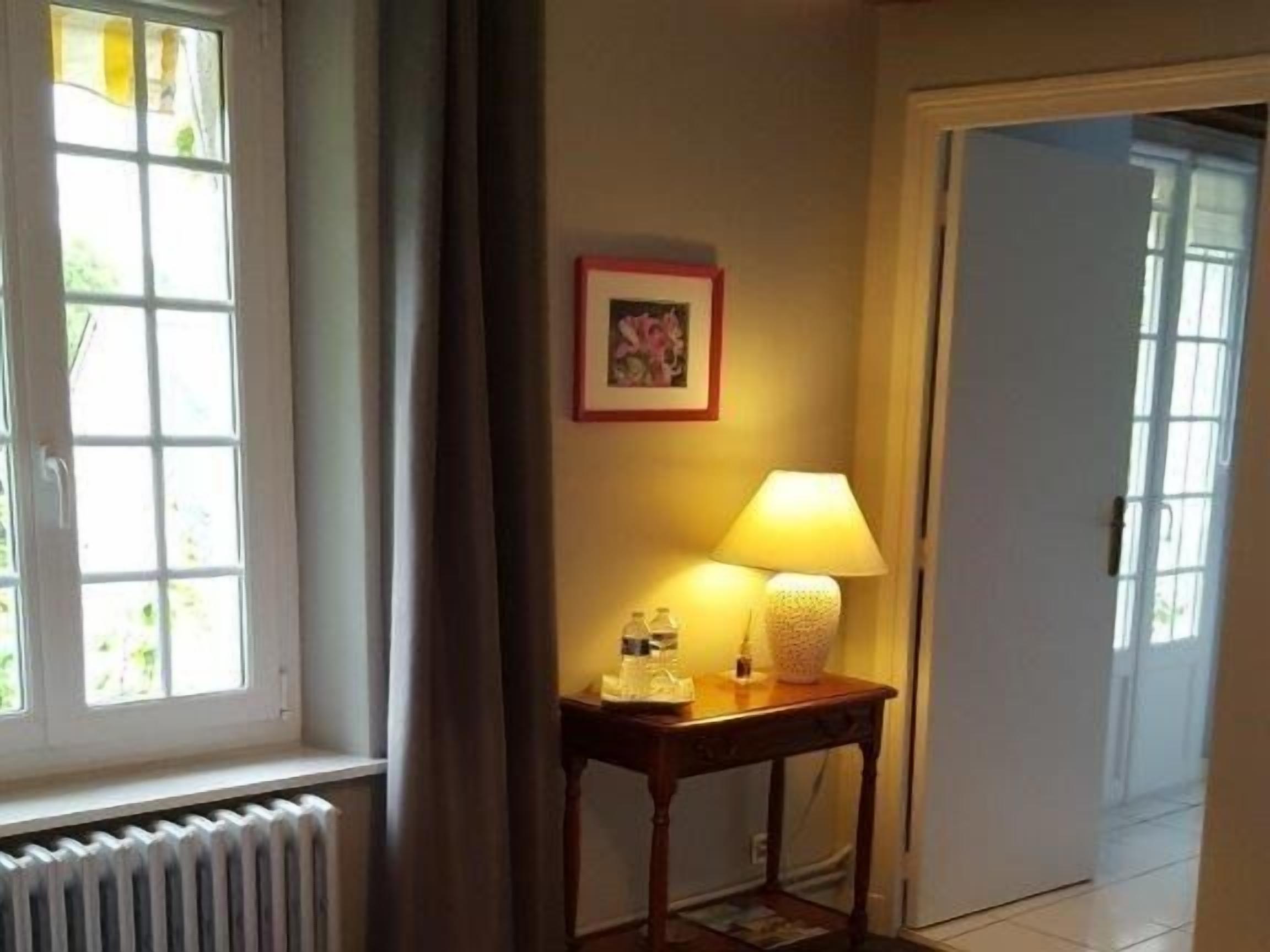A room with a radiator, a table with a lamp, a framed picture on the wall, and a door.