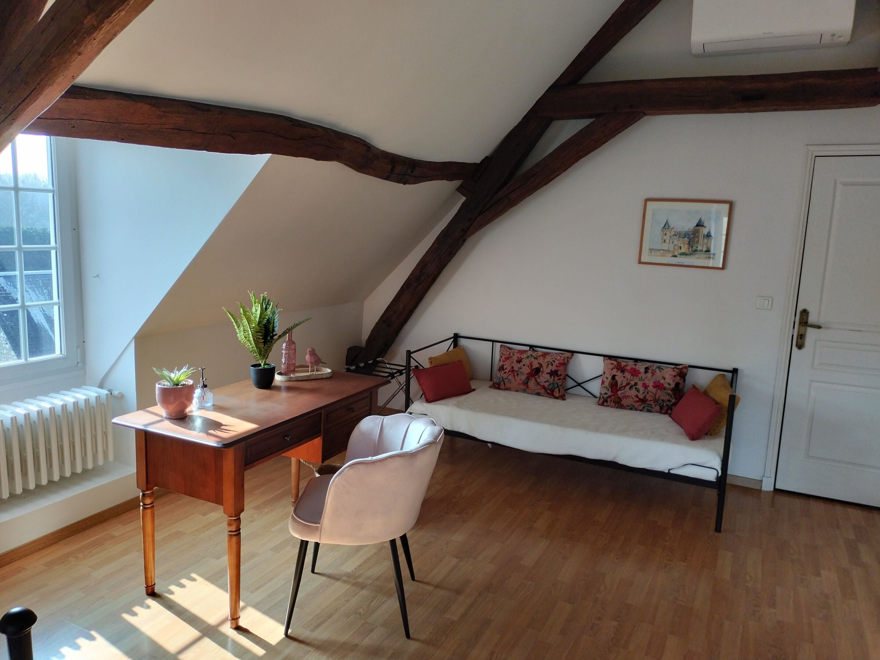 Acogedor dormitorio en ático con un escritorio de madera, una silla, un sofá con cojines estampados y un radiador.