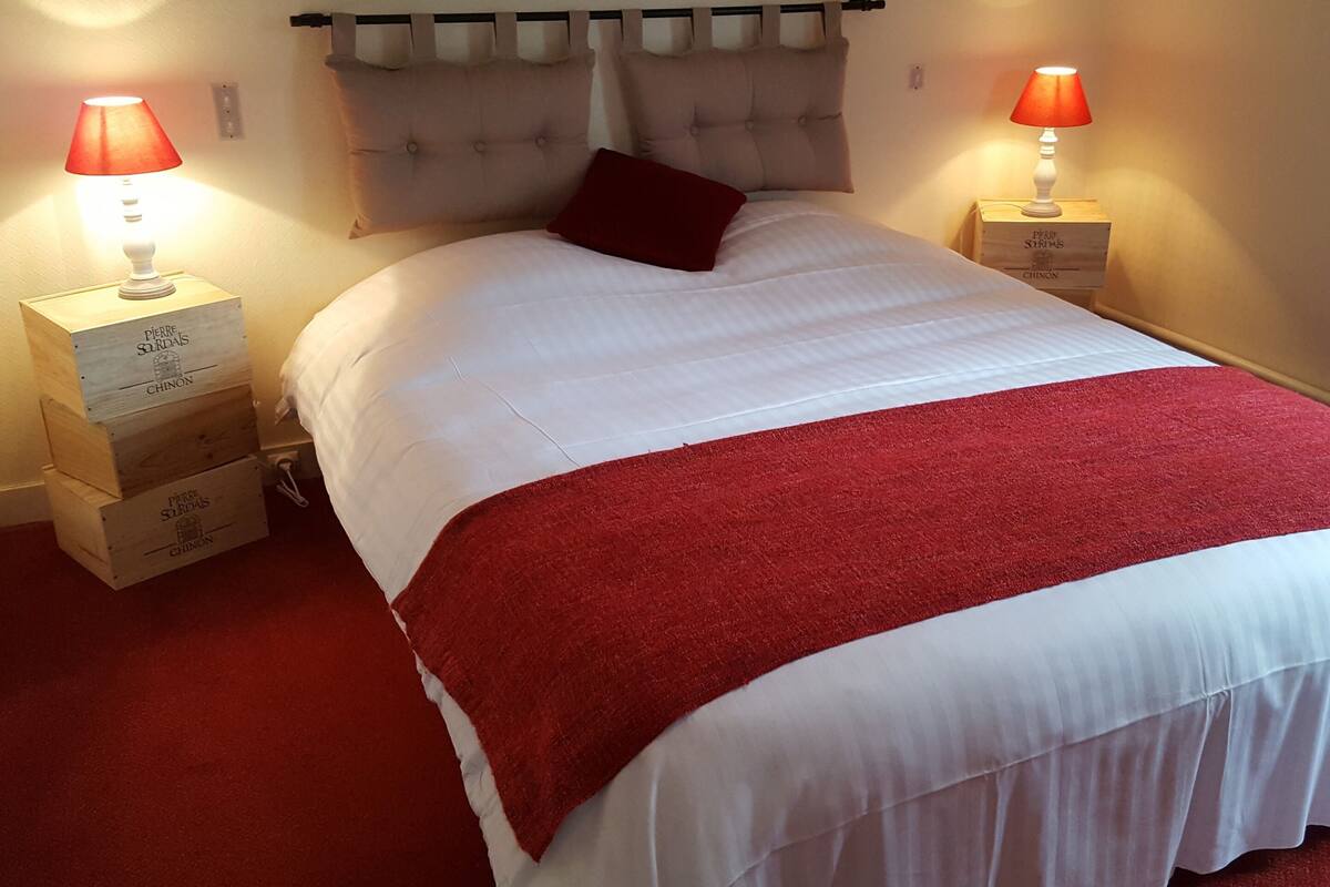 A neatly made bed with a red throw blanket, two bedside lamps, and wooden nightstands with writing on them.