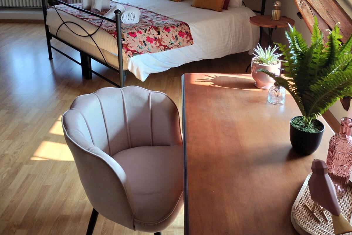 A cozy attic bedroom with a bed, a chair, a table, and a potted plant.