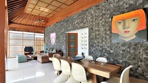 A modern dining area with a wooden ceiling, a stone wall, and a large painting. - Villa Flores (Seminyak)