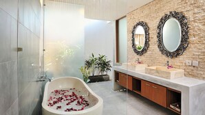 A modern bathroom with a freestanding bathtub, two sinks, and decorative mirrors on a brick wall. - Villa Flores (Seminyak)