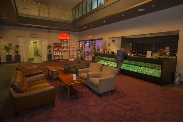 A lobby with leather sofas, a reception desk, and a glass railing. - Hotel Safir Casino (Sezana)
