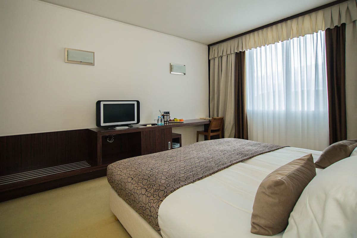 Habitación de hotel con cama, escritorio, televisión y ventana con cortinas.