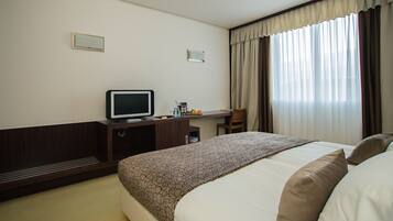 Habitación de hotel con cama, escritorio, televisión y ventana con cortinas.