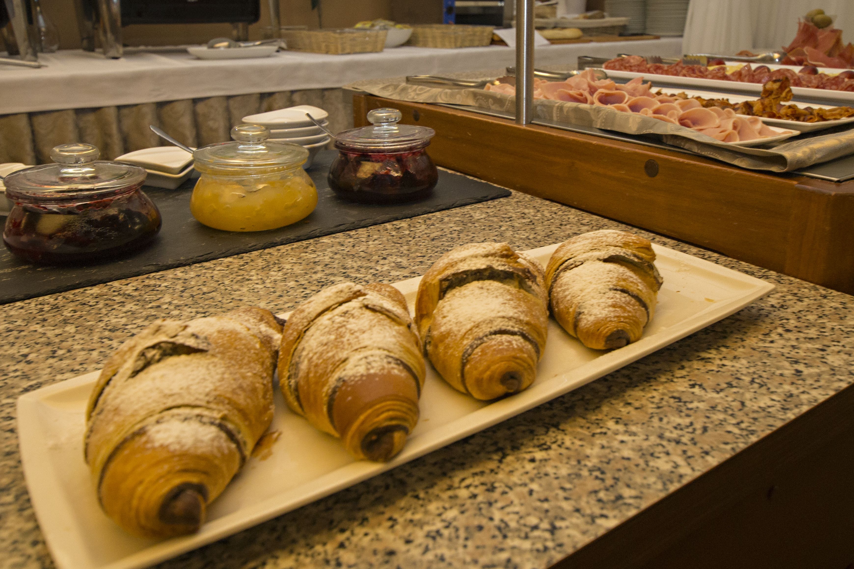 Un buffet con dolci, tra cui croissant, e diversi condimenti su un piano di granito.