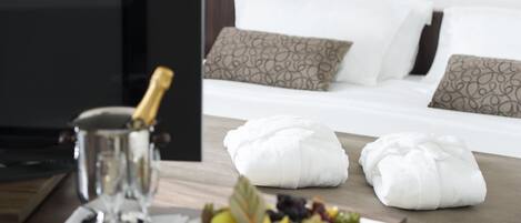 A neatly arranged breakfast table with a fruit platter, a bottle of champagne, and two white towels.
