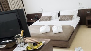 Hotelkamer met een bed, een televisie, een nachtkastje met een champagnefles, een schaal fruit en slippers.
