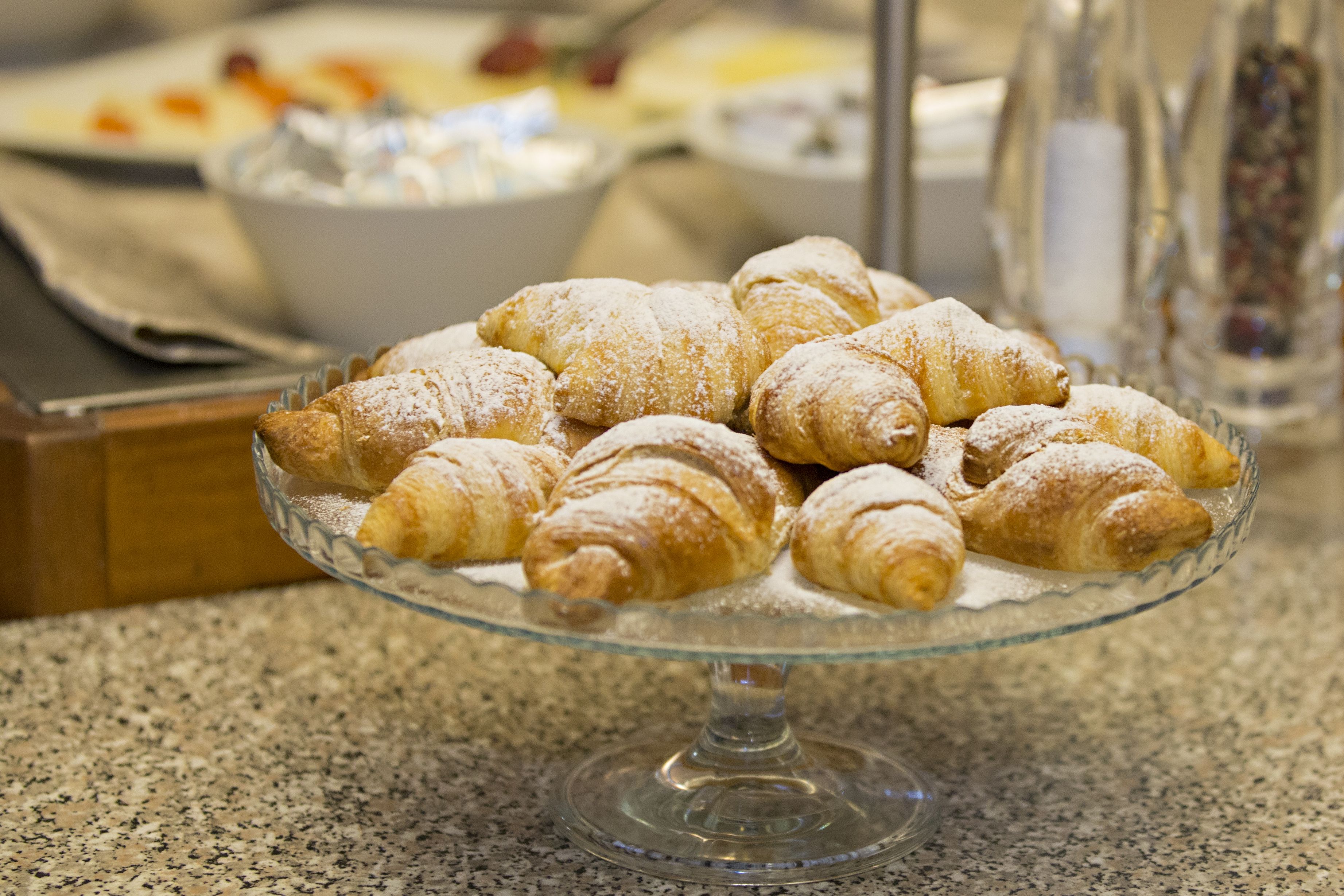 A glass serving dish with croissants on a granite countertop.