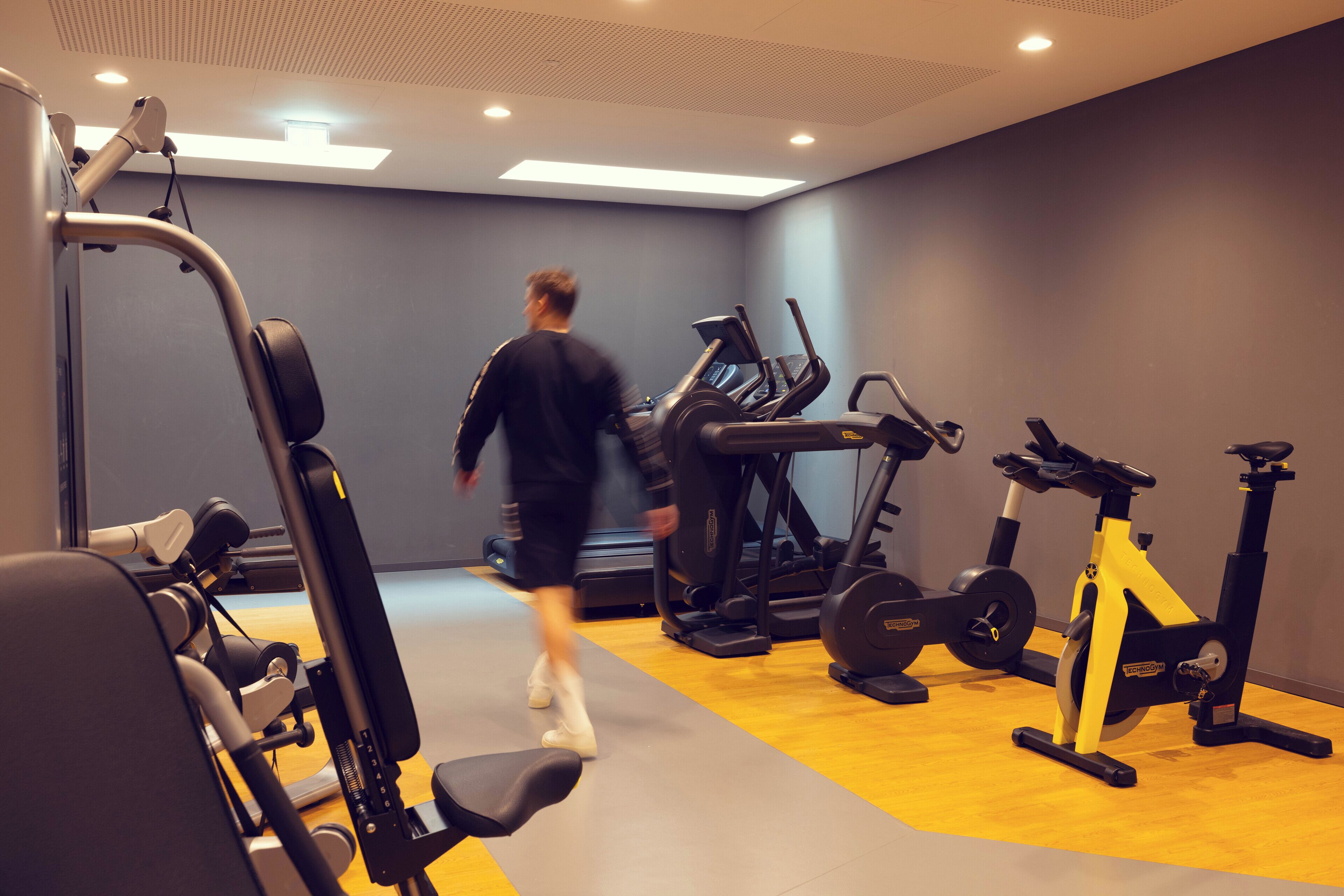 Ett gym med olika typer av träningsutrustning, inklusive löpband, motionscyklar och styrketräningsmaskiner.