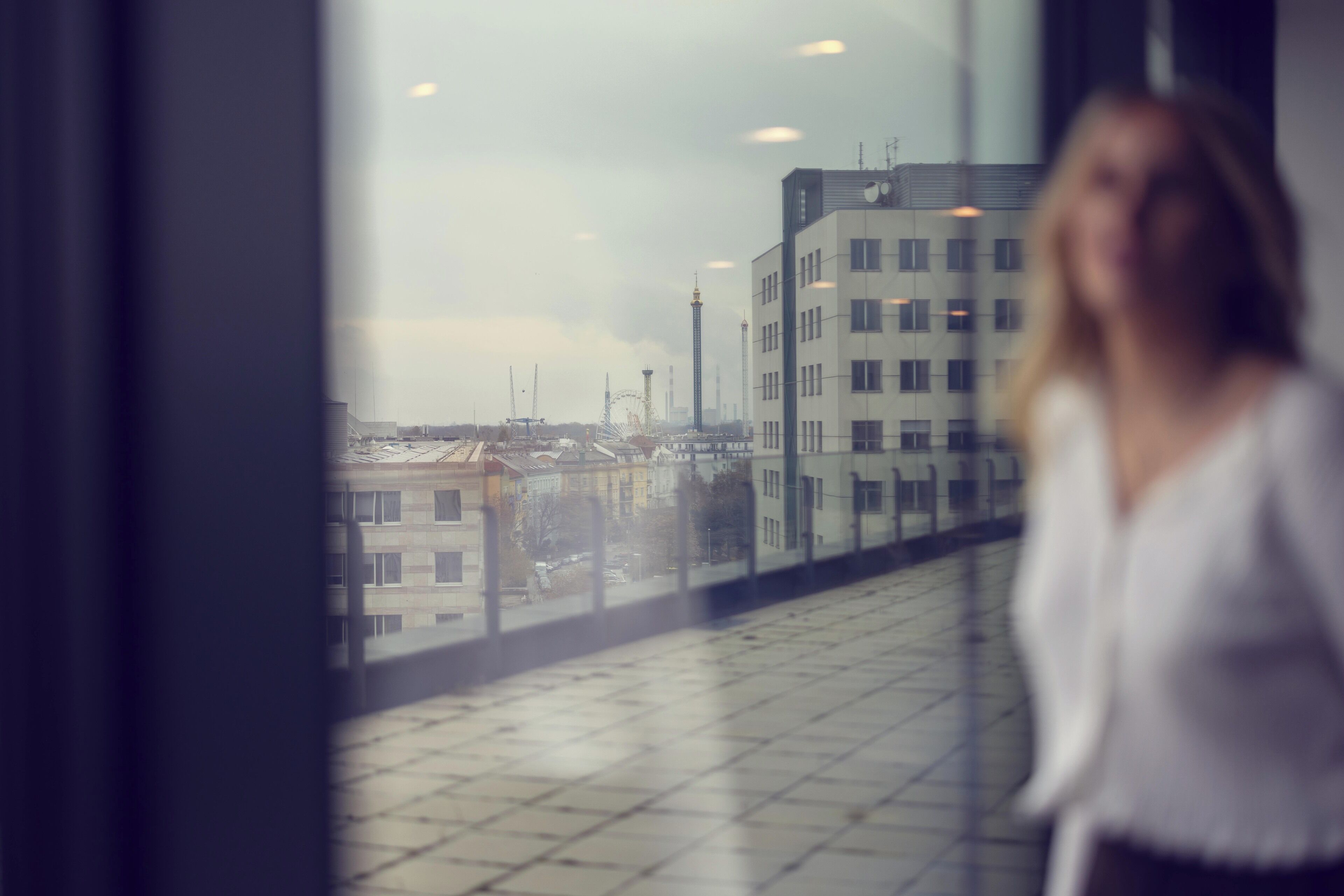 Una mujer de pie junto a una ventana con vistas a un paisaje urbano con edificios y una torre.