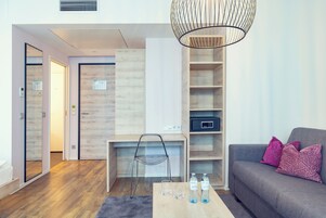 Uma sala de estar moderna com sofá, mesa de centro com copos e garrafas de água, escrivaninha com cadeira e estante embutida.