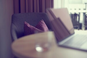 Quarto moderno com um laptop sobre uma mesa, uma cadeira com almofadas estampadas e uma janela com persianas.
