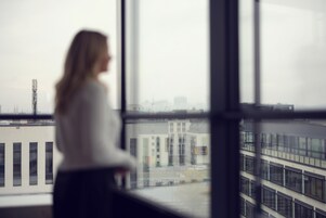 Una persona de pie junto a una ventana con vista a un conjunto de edificios.