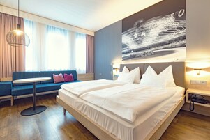 Habitación de hotel moderna con una cama grande, una mesa redonda, un sofá y un cuadro en la pared.