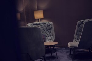 Quarto com duas poltronas estofadas, uma mesa redonda pequena e um abajur.