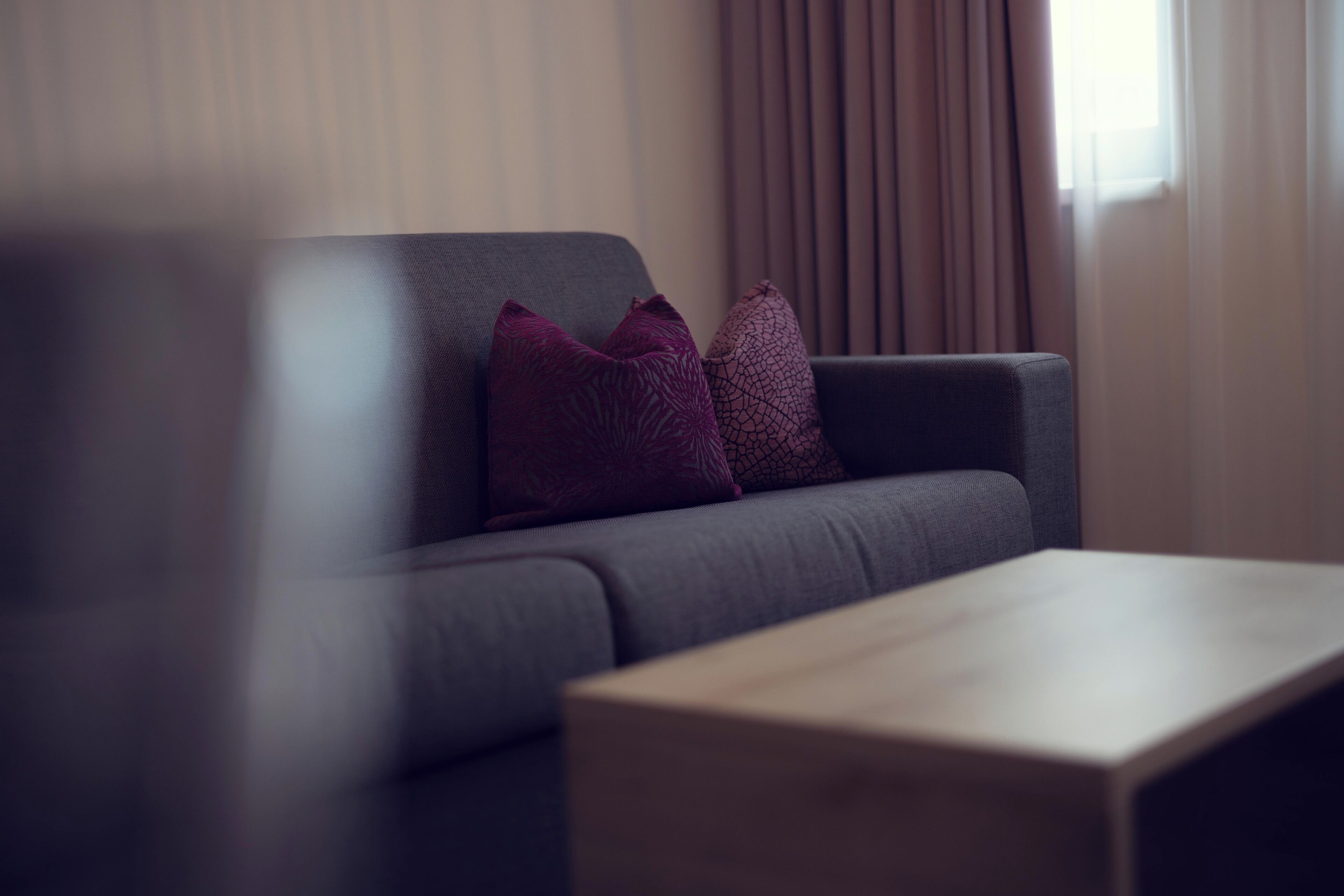Ein modernes Wohnzimmer mit einem grauen Sofa, zwei violetten Kissen und einem Holztisch.