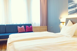 Quarto de hotel com cama, sofá e luminária.