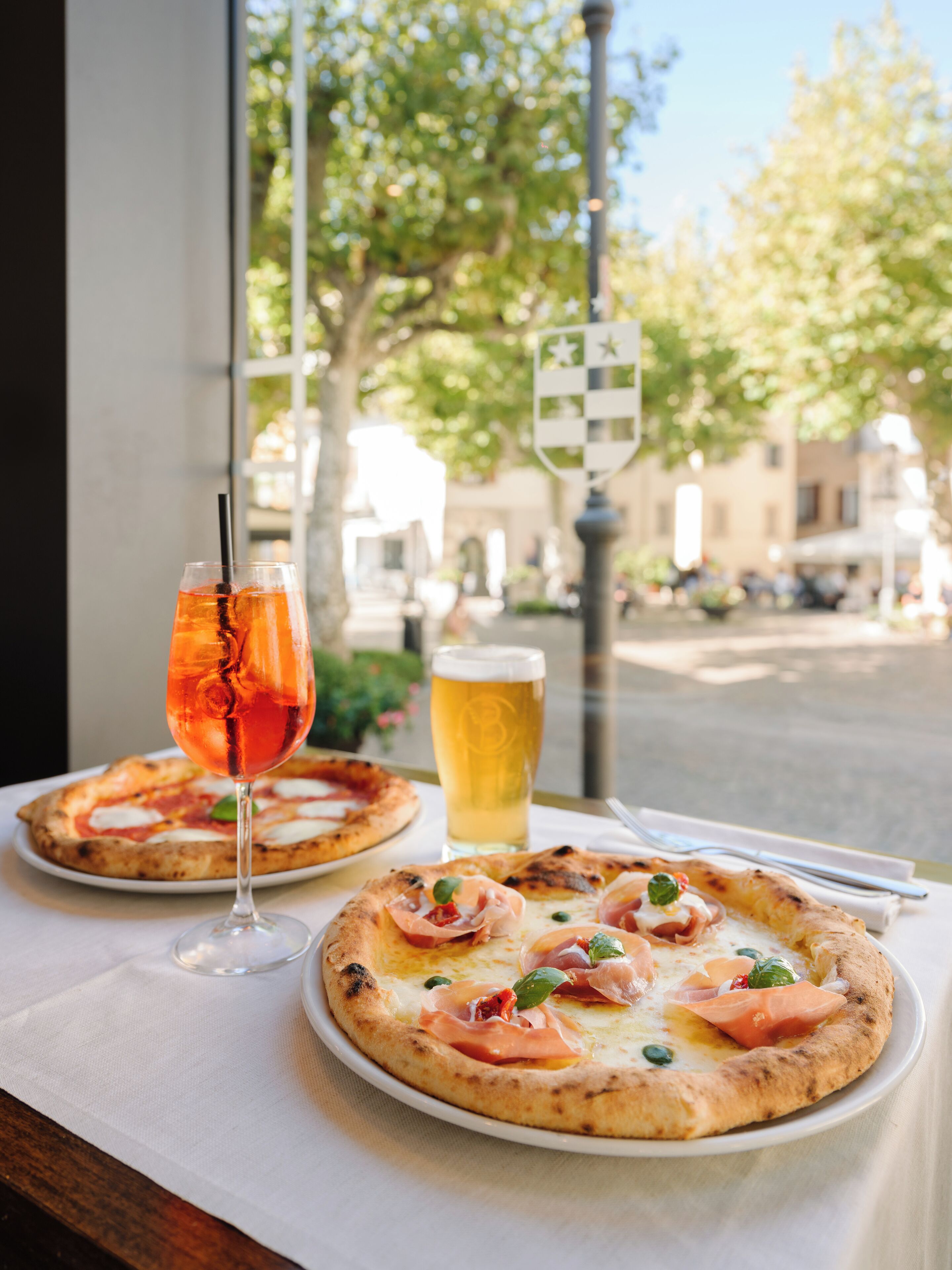 Dos pizzas sobre una mesa con una bebida y una jarra de cerveza.
