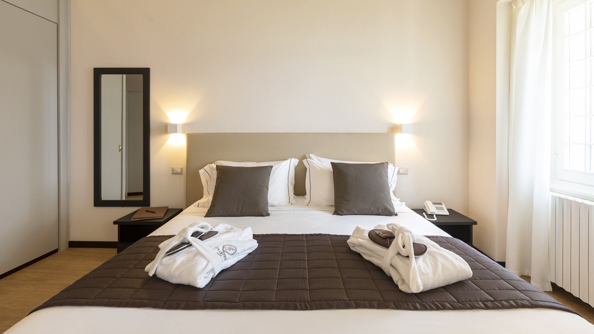 Una habitación de hotel con una cama, dos mesitas de noche, un tocador, un espejo y una ventana.