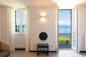 Una habitación con vistas a un lago y montañas, una lámpara redonda montada en la pared, una mesa negra y un radiador.