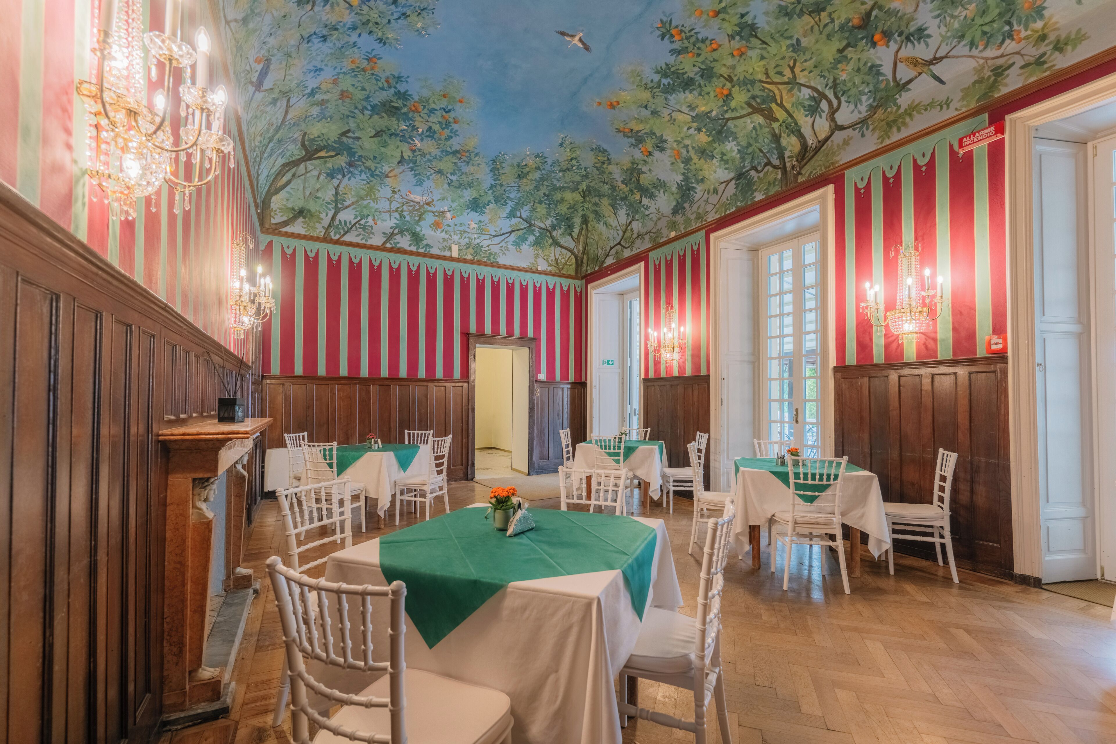 Comedor con paneles de madera, manteles verdes, sillas blancas y un mural en el techo.