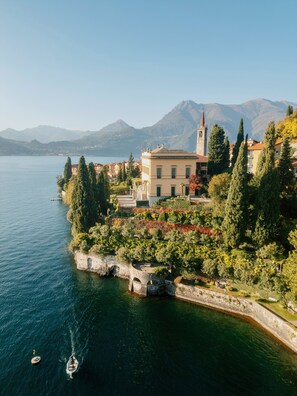 A lakeside property with a prominent building, a stone pathway, and a view of the lake and mountains. - Hotel Villa Cipressi - by R Collection Hotels (Varenna)