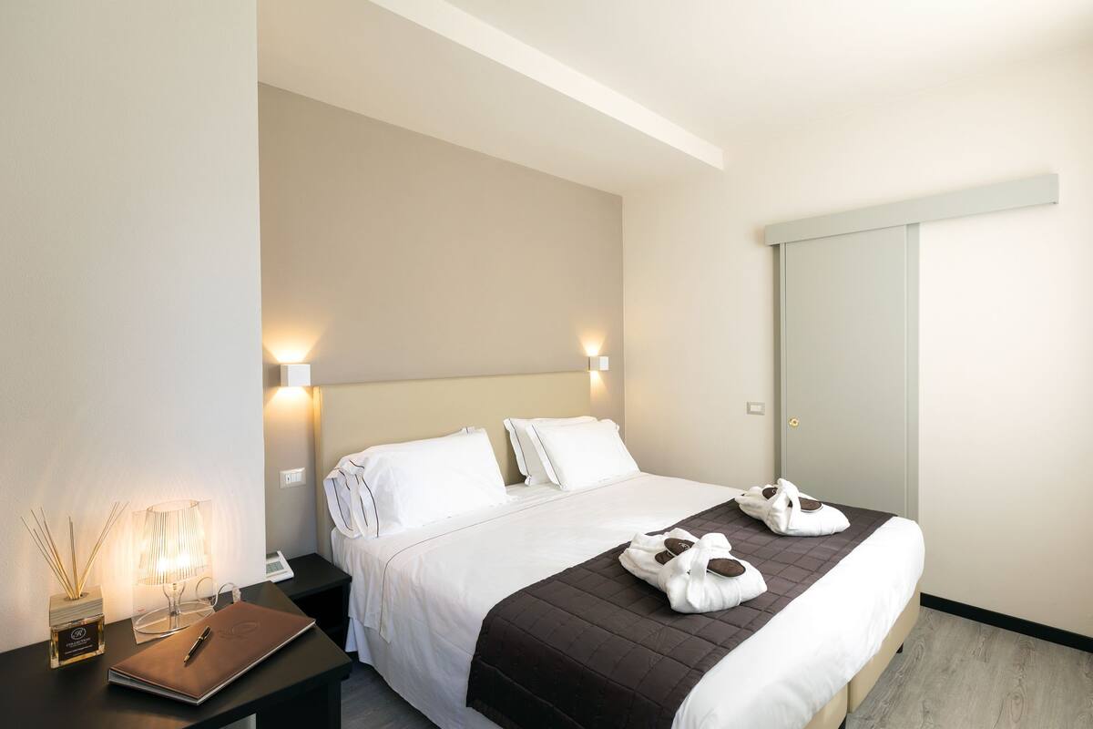 A hotel room with a bed, bedside tables, a lamp, a bottle of perfume, and a notebook.