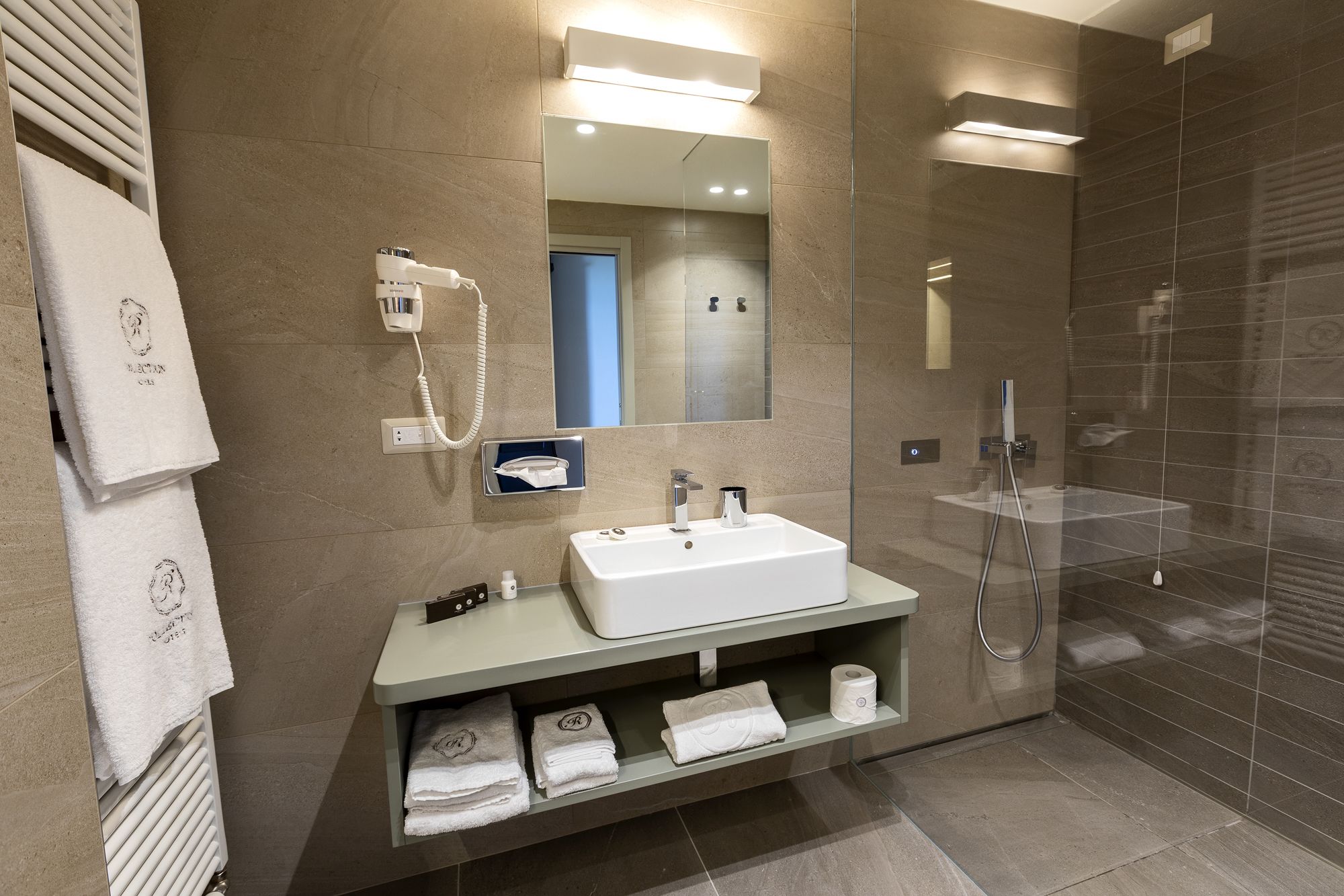 Une salle de bain moderne avec un grand miroir, un lavabo blanc, un porte-serviettes et une douche à parois de verre.