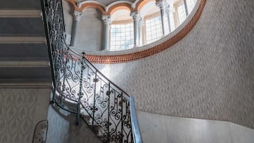 A grand staircase with ornate railings, a patterned floor, and a vaulted ceiling.