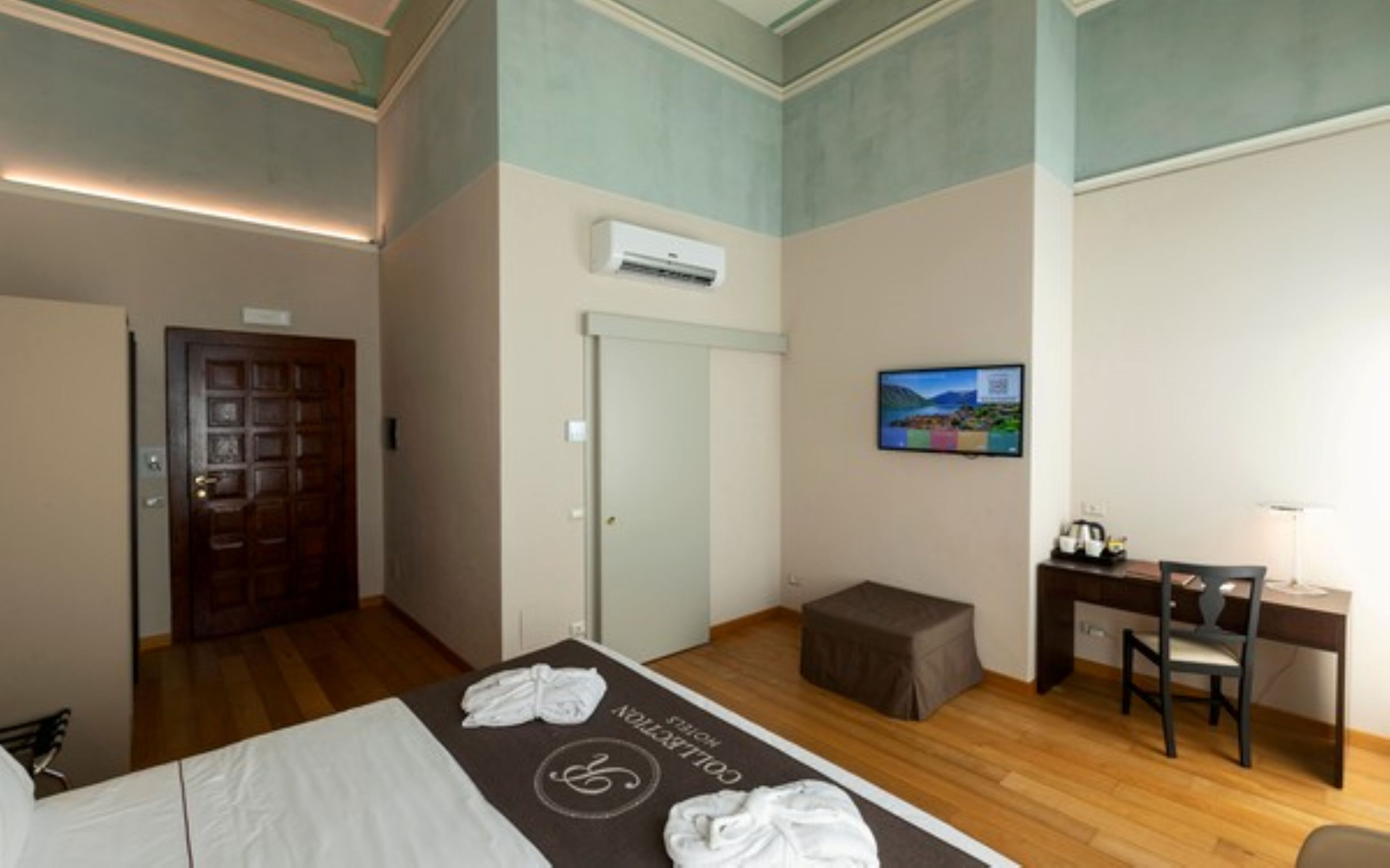 Een hotelkamer met een bed, een bureau, een stoel, een airconditioningapparaat en een televisie aan de muur.