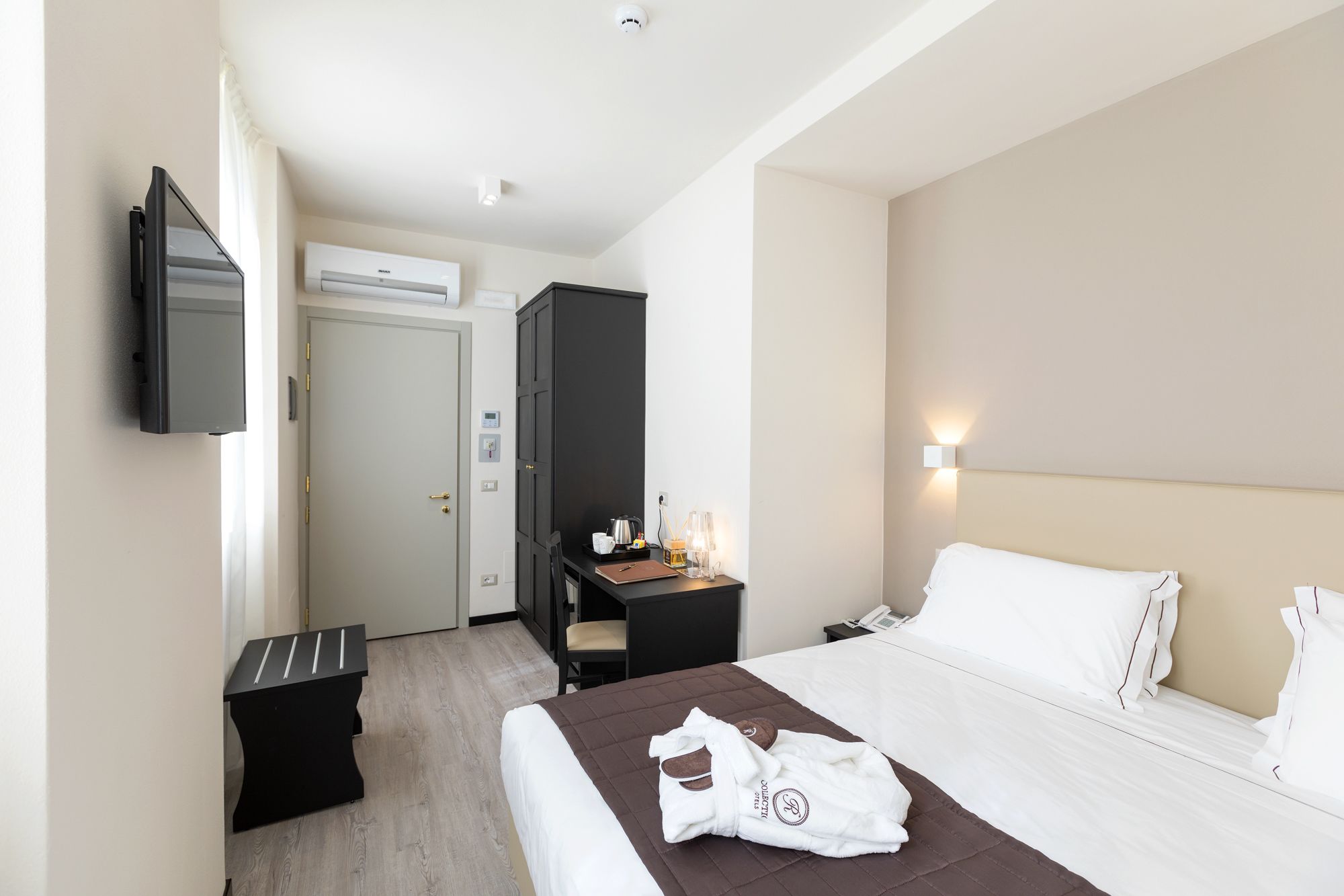 A hotel room with a bed, a desk, a chair, a TV, and a wardrobe.