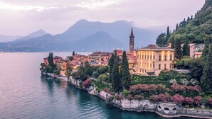 Un pueblo a orillas del lago con edificios históricos, una torre destacada y un puente de piedra.