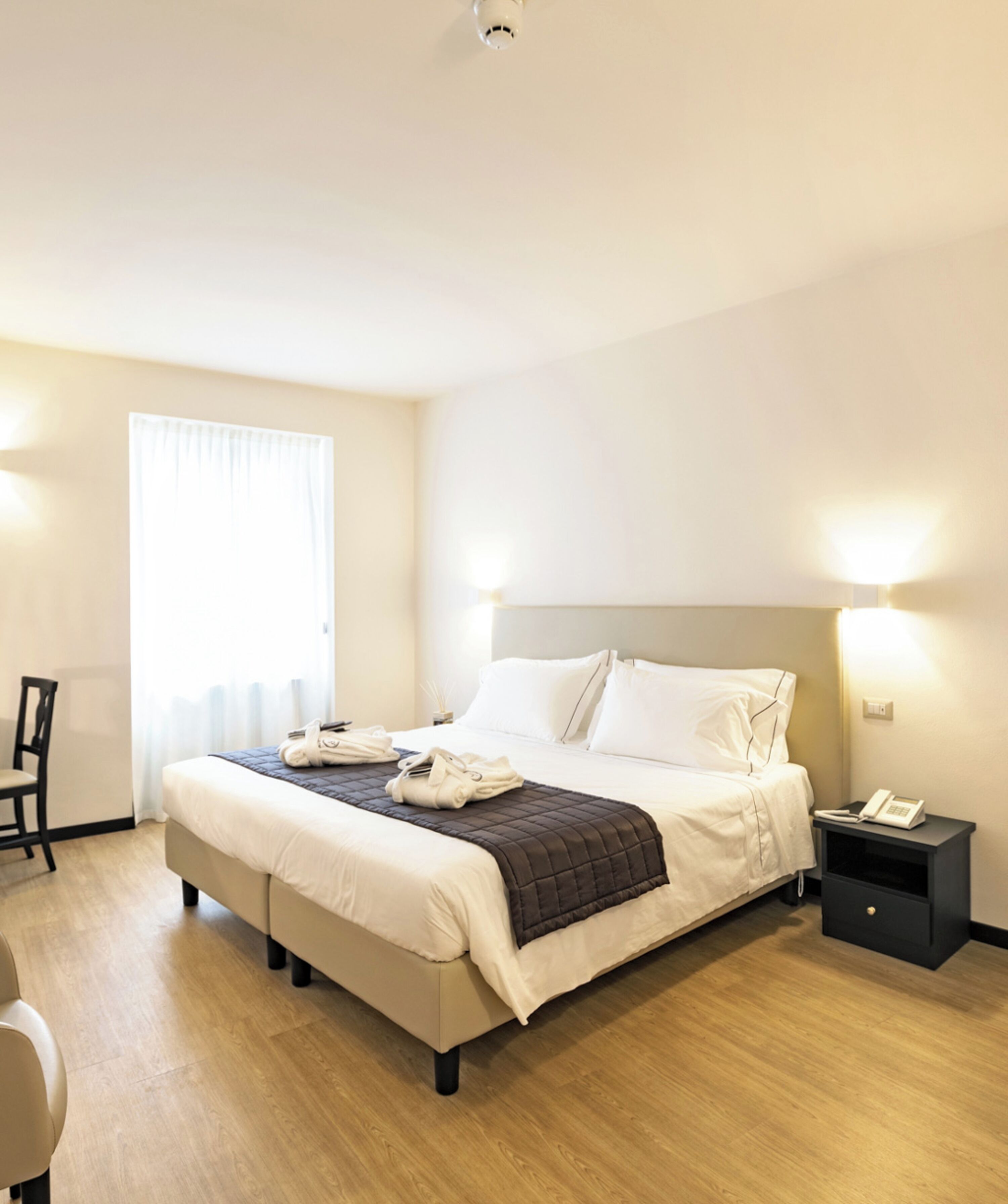 A hotel room with a bed, bedside tables, a chair, and a window with curtains.