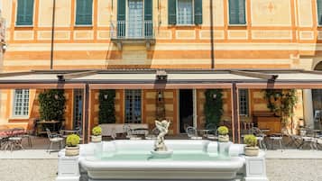 Ein Gebäude mit überdachter Außenbestuhlung, einem Brunnen sowie Tischen und Stühlen im Freien.