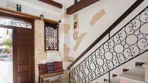 Una escalera con barandales negros ornamentados, un banco de madera con cojines estampados y un muro de piedra con detalles decorativos.