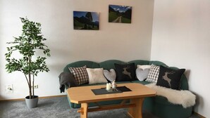 Un salon chaleureux avec un canapé vert, une table basse en bois, une plante en pot et deux tableaux accrochés au mur.
