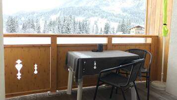 A balcony with a table and chairs, a view of snow-covered mountains, and a wooden railing.