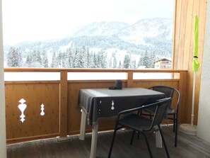 Ein Balkon mit Tisch und Stühlen und Blick auf schneebedeckte Berge, versehen mit einem Holengeländer.