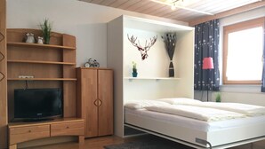 Une chambre moderne comprenant un lit, une télévision, une armoire et une étagère murale agrémentée d’objets décoratifs.