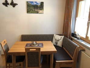 Un coin repas avec une table en bois, des chaises, un banc, un coussin orné d’une tête de cerf, un chandelier et un tableau représentant un paysage accroché au mur.