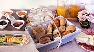 Un bufé de desayuno con panes, bollería y frutas variadas.