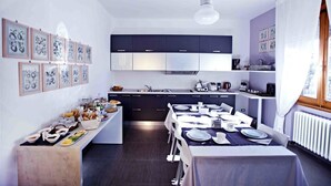 A modern kitchen with a dining area, featuring a long counter with breakfast items, a dining table set for four, and a hanging light fixture.