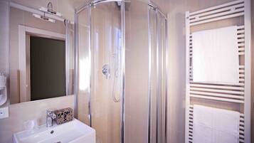Un baño moderno con ducha de vidrio, lavamanos blanco y toallero.
