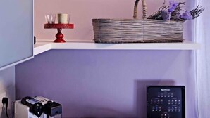 A kitchenette with a coffee machine, a tray of dishes, and framed botanical illustrations on the wall.