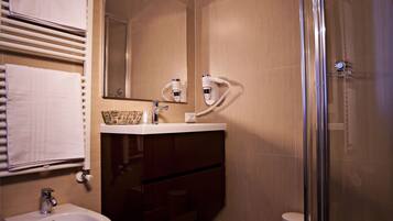Un baño moderno con un bidé, una ducha con cerramiento de vidrio, un tocador con espejo y un perchero para toallas.
