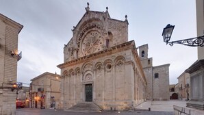 A historic building with a large arched entrance, a clock tower, and a bell tower. - Svegliarsi nei Borghi - La Patronale (Troia)