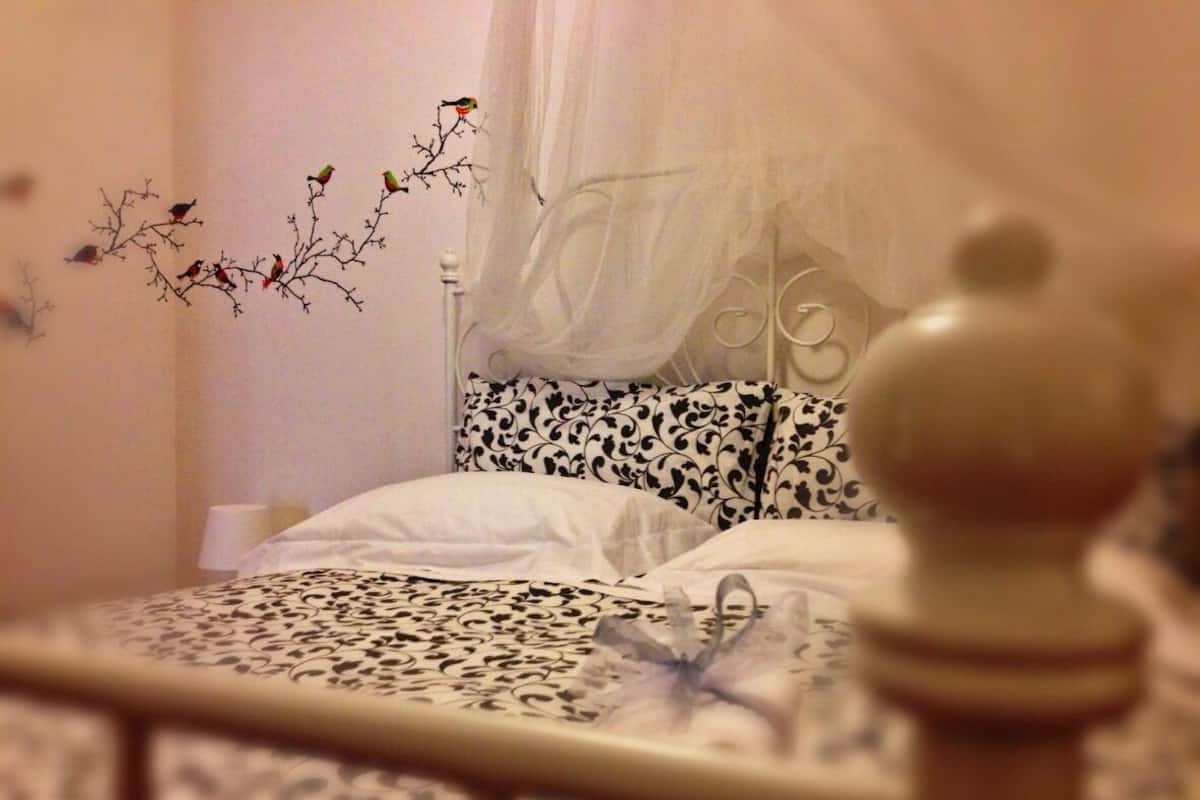 A bedroom with a bed, a canopy, and a wall decoration of birds on branches.
